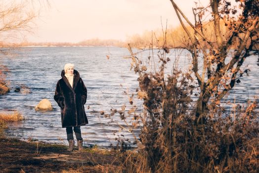 A mature woman wearing a warm fur coat and a woolen cap stays close to the Dnieper river in Kiev, Ukraine, during winter