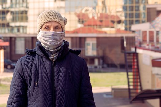 A poor elderly woman wears a homemade mask to protect herself from viruses such as coronavirus, also known as covid-19, or SARS and MERS. She's in an urban environment