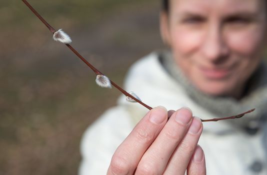 A woman is holding a willow branch in her hand and looking a catkin at the beginning of spring