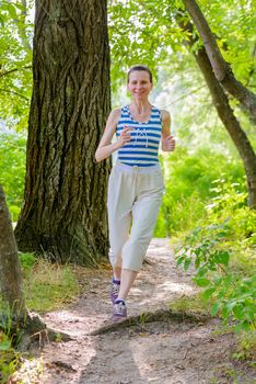 A happy senior woman is running in the forest close to the lake during a warm summer day