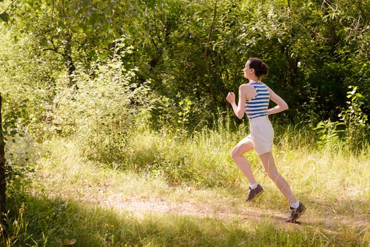 A happy senior woman is running toward the light in the forest during a warm summer day