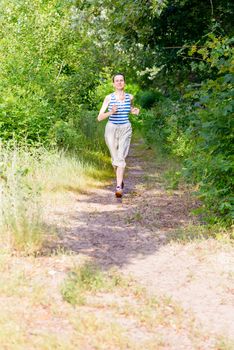 A happy senior woman is running in the forest during a warm summer day