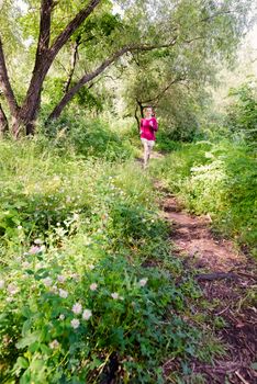 A happy senior woman is running toward the nature in the forest during a warm summer day