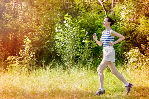 A happy senior woman is running toward the light in the forest during a warm summer day