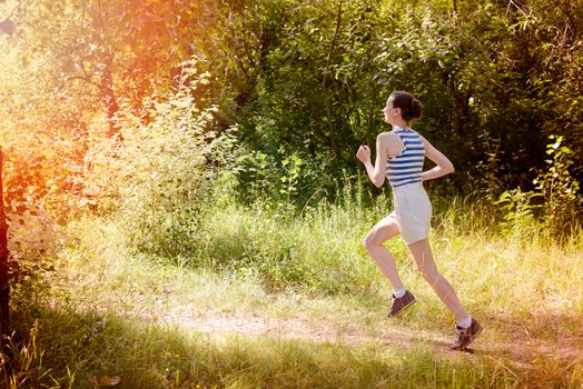 A happy senior woman is running toward the light in the forest during a warm summer day
