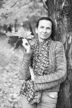 Black and white portrait of a smiling adult caucasian woman is picking yellow maple leaves in autumn in the park