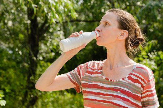 A senior woman is drinking water or yogurth to quench her thirst after a long run in the forest