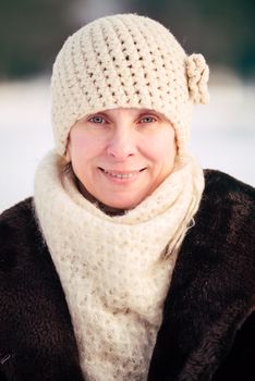 A winter portrait of a smiling senior adult woman wearing a wool cap and a scarf, with a snow background