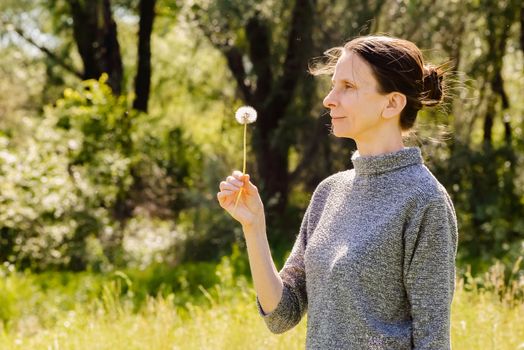 Adult woman blowing the seeds of a dandelion flower at the end of spring near to the forest