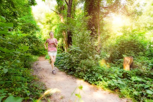 A happy senior woman is running toward the light in the forest during a warm summer day