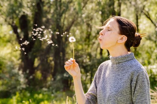 Adult woman blowing the seeds of a dandelion flower at the end of spring near to the forest