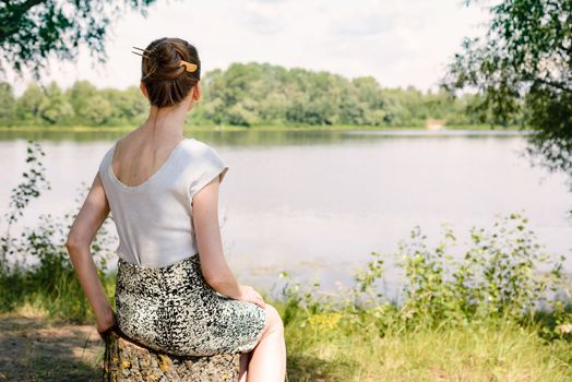 A woman is sitting close to the Dnieper river in Kiev, Ukraine, and is watching or observing far in the distance, under a warm and soft summer sun