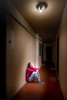 A sad and desperate woman sits in a dark corridor illuminated by a gloomy light. Her pain and her many problems pushed her into complete isolation. His sadness is only equalled by his loneliness.