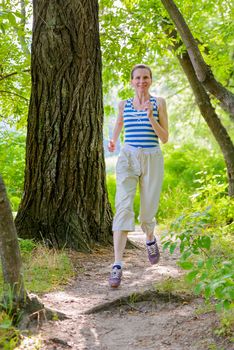 A happy senior woman is running in the forest close to the lake during a warm summer day