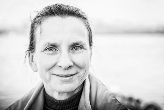 A warm black and white portrait of a nice senior woman close to the river