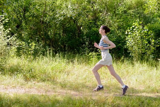 A happy senior woman is running toward the light in the forest during a warm summer day