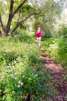 A happy senior woman is running toward the nature in the forest during a warm summer day