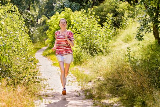 A happy senior woman is running toward the light in the forest during a warm summer day