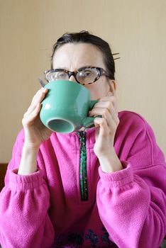 A mature woman with glasses wearing a pink pull-over and drinking coffee in a green cup at morning for breakfast