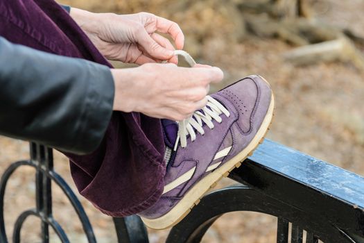 A woman is tying her violet shoes with white laces, during a warm hiking day in mountain