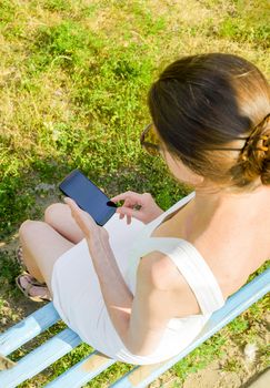 A senior woman sits on a woden bench and used a smartphone to send a text message