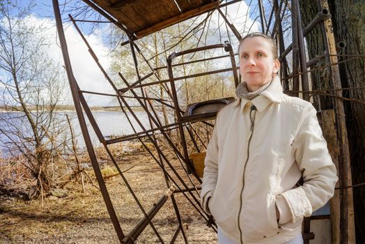 A nice adult woman standing close to the river at the beginning of spring observes something in the distance