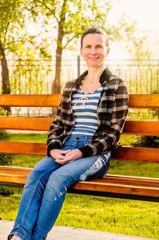 A nice senior mature woman sitting on a wooden bench at sunset