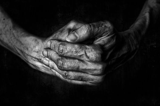 Black and White photo of senior woman hands praying on a dark background texture