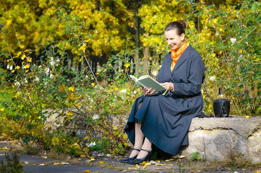 Sexy senior woman reading a book in the park during a sunny autumn day