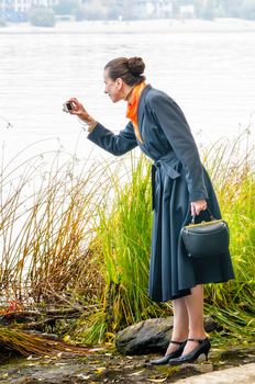 Elegant senior business woman with a digital camera, a bag and an orange scarf, taking pictures along the river