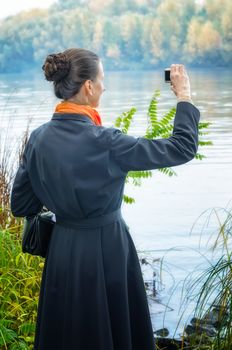 Elegant senior business woman with a digital camera, a bag and an orange scarf, taking pictures along the river