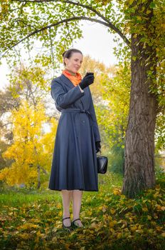 Senior business woman with a mobile phone, a bag and an orange scarf, walking in the park, under the trees in autumn