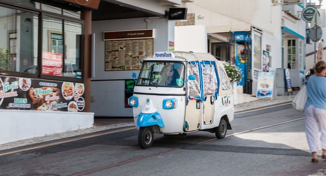 Albufeira, Portugal - May 3, 2018: Tuk Tuk carrying tourists traveling on a street in the historic city center on a spring day