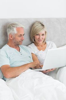 Portrait of a happy mature couple using laptop in bed at home