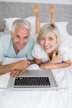 Portrait of a relaxed mature couple using laptop in bed at home