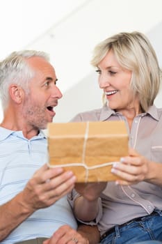 Portrait of a smiling woman surprising mature man with a gift on sofa at home