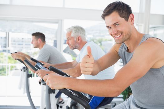 Portrait of happy man on exercise bike gesturing thumbs up at gym