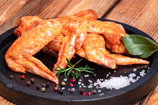 Raw chicken wings in a marinade with spices on a black plate. Top view. Chicken meat close-up.