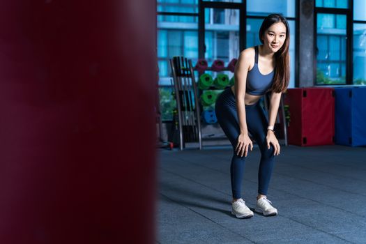 Asian Women rest during exercise. She's holding her hand at Knee with blur Racks Fitness Equipment background xhaustion and being alone at the gym sport and healthy concept
