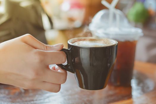 Hold hot coffee, heart shape with milk latte on top of black ceramic cup on hand at coffee shop and cafe in vintage tone, copy space for your text. Times to relax with caffiene concept.