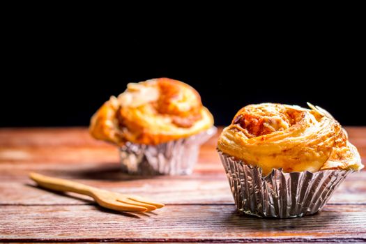 Delicious homemade almond danish bread in foil cup on a wooden table in the home kitchen on black background.