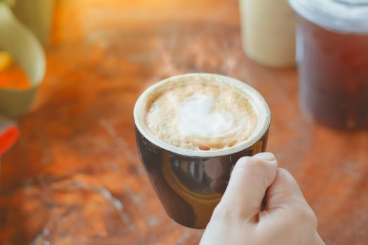 Hold hot coffee, heart shape with milk latte on top of black ceramic cup on hand at coffee shop and cafe in vintage tone, copy space for your text. Times to relax with caffiene concept.