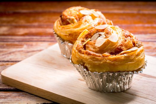 Delicious homemade almond danish bread in foil cup on a wooden chopping board and table in the home kitchen on black background.