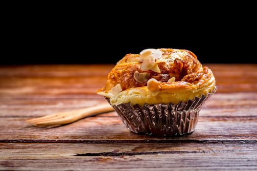 Delicious homemade almond danish bread in foil cup on a wooden table in the home kitchen on black background.