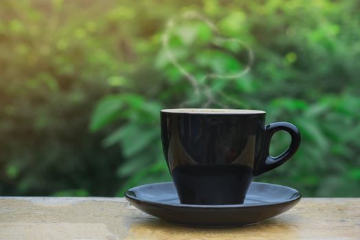 Hot coffee, heart shape with milk latte on top of black ceramic cup on wooden table in coffee shop and cafe with green background, copy space for your text. Times to relax with caffiene concept.