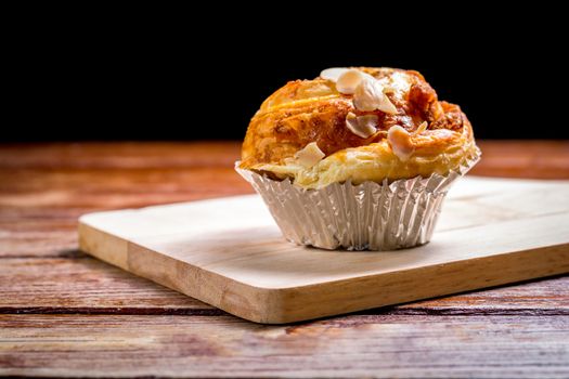 Delicious homemade almond danish bread in foil cup on a wooden chopping board and table in the home kitchen on black background.