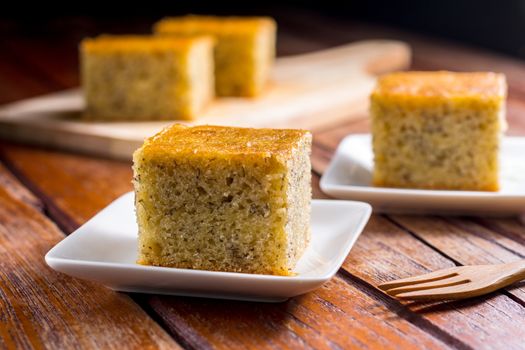 Close up square cut of homemade sweet and solf banana cake on white plate on wooden table. Delicious and healthy bakery.