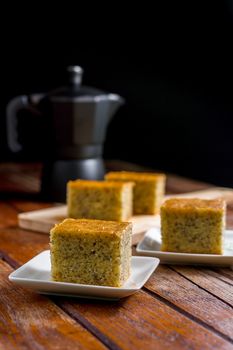 Close up square cut of homemade sweet and solf banana cake on white plate on table with solf focus black moka pot. Delicious and healthy bakery.