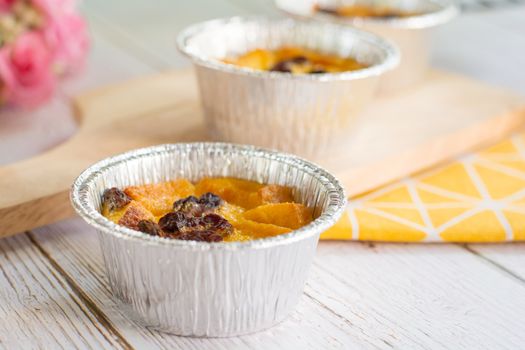 Bread pudding with black rasins in round foil cup on wooden tray. Delicious custard for coffee times.