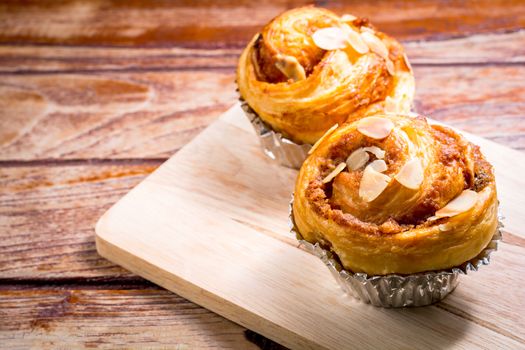 Delicious homemade almond danish bread in foil cup on a wooden chopping board and table in the home kitchen on black background.